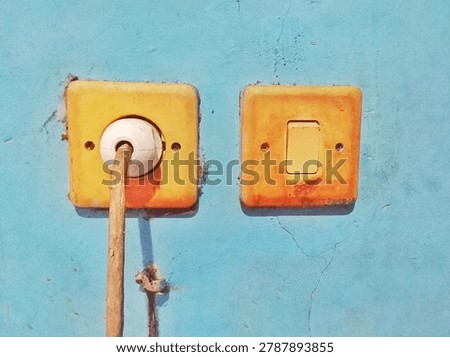 Old Yellow Electrical Socket with Plug and Switch Mounted on Weathered Blue Wall