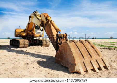 Old yellow excavator working on sand beach with sea and boat Background.