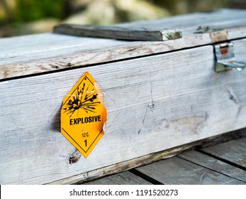 Old Yellow Explosive Hazardous Pictograph Sign On Wooden Grungy Weapon Military Chest Box. Danger Warning Sign For Propellant Explosive Substance With A Blast Hazardous Materials Class 1.2 