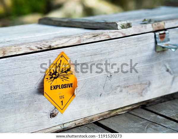 Old\
yellow explosive hazardous pictograph sign on wooden grungy weapon\
military chest box. Danger warning sign for Propellant explosive\
substance with a blast hazardous materials class 1.2\

