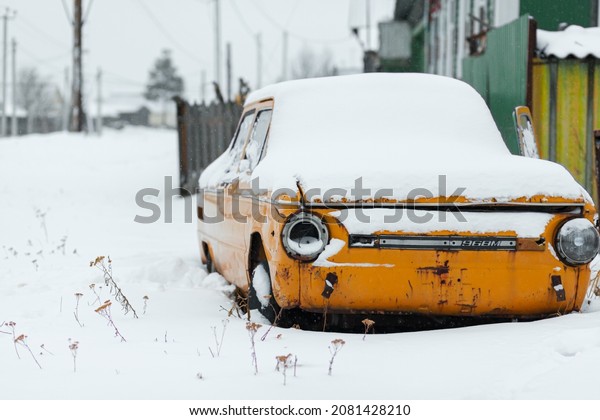 Old yellow wrecked car in vintage style. Abandoned\
rusty yellow car. of the headlights of the front view of a rusty,\
broken, abandoned car near the house. Russia, Kemerovo Region,\
November 25, 2021