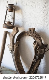 An old yoke for harnessing draft horses, used on the farm. A horse yoke hangs on a white wall against the background of an old kerosene lamp. Old stable accessories - Shutterstock ID 2206722849