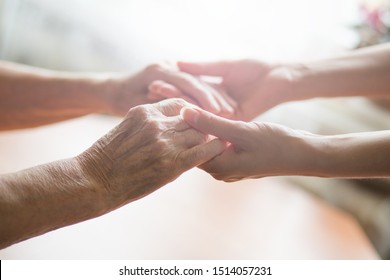 Old and young holding hands on light background. Young and old generation. Helping hands. Care for the elderly concept