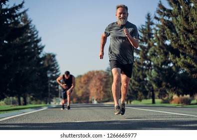 The Old And Young Sportsmen Jogging On The Road