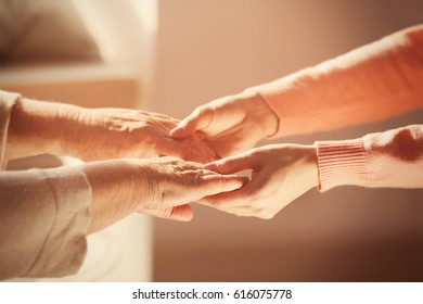 Old And Young Women Holding Hands On Blurred Background, Closeup