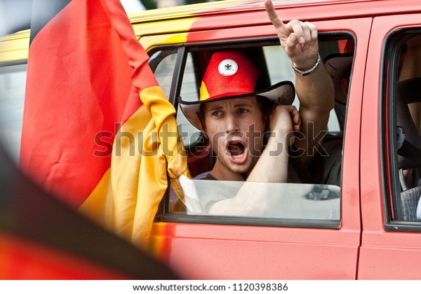 Oldenburg,\
Germany - July 03, 2010: Man with hat in german colors and big\
german flag looks out of a car window and shouts to celebrate a\
victory of the german soccer team in world\
cup