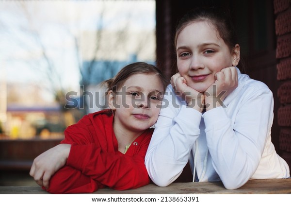 Older 10-year-old and younger 7-year-old sister\
on   porch of house in village.\
