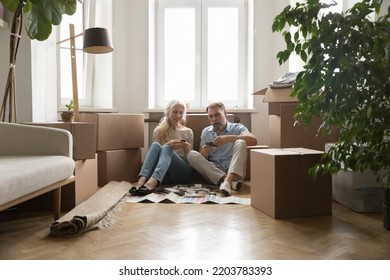 Older 60 Couple Of New Homeowners Choosing Wall Decoration Colors, Reviewing Samples, Planning New Interior Design After Relocation, Sitting On Floor At Moving Paper Boxes