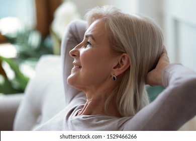 Older 60s Woman Put Hands Behind Head Resting Seated Indoors Enjoy Summer Day Looking Out Window Close Up Pretty Face Side View, No Stress, Free Time, Serene Calm Person, Keep Calm, Take Break Concept