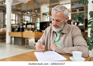 Older Adult Business Man Writing In Notebook, Middle Aged Author Or Writer Taking Notes Thinking Of New Ideas, 50s Mature Male Student Making Checklist, Studying Or Learning In Cafe Sitting At Table.