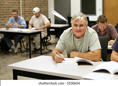 An Older Adult Education Student Takes School Seriously While The Younger Guys Are Goofing Off Making Paper Airplanes.