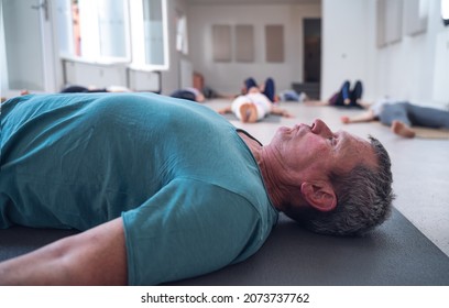 Older Adult Male Lying On The Floor During A Group Yoga Class.