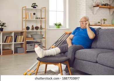 Older Adult With Physical Injury At Home: Sad Senior Man With Broken Leg In Plaster Cast Sitting On Sofa And Making Phone Call On Mobile To Talk To Doctor About Bone Fracture Or Share News With Family