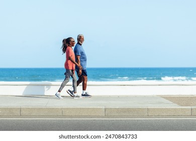 An older African American couple enjoys a peaceful, joyful walk together along a seaside promenade, showcasing active senior lifestyle and companionship. - Powered by Shutterstock