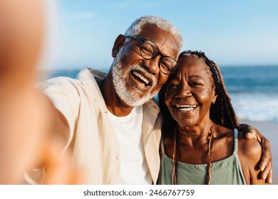 An older African American couple shares a joyful moment while taking a selfie on a sunny seaside promenade. Their happiness and affection are evident as they smile broadly. - Powered by Shutterstock