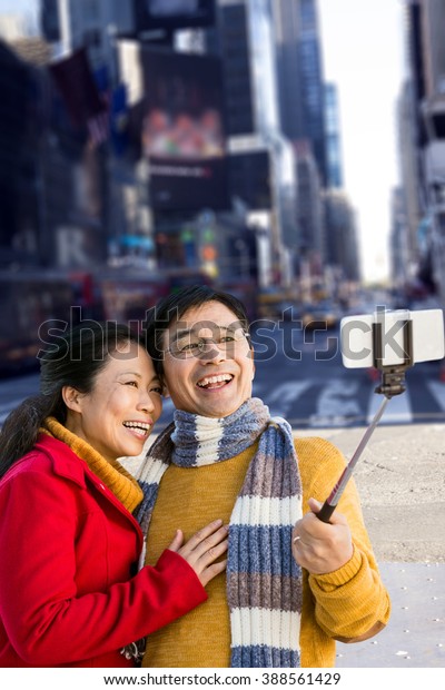 Older asian couple on balcony taking selfie against\
picture of a city