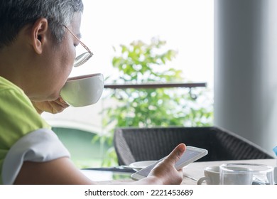 Older Asian eyeglass drinking coffee and looking Smartphone searching information when relax time at co-working space or café - Powered by Shutterstock