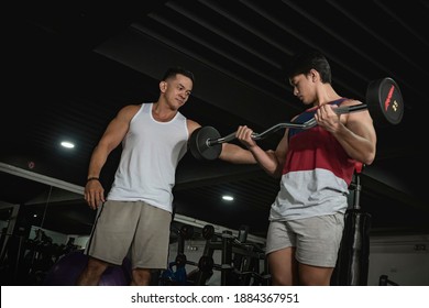 An Older Asian Guy Teaches A Young Man Proper Bicep Curls At The Gym. Working Out, Training Biceps At The Gym.