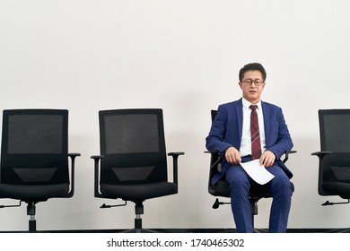 Older Asian Job Seeker Preparing For Interview With Eyes Closed While Waiting In Line