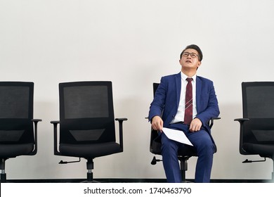 Older Asian Male Job Seeker Looking Up To The Ceiling While Waiting In Line For Interview