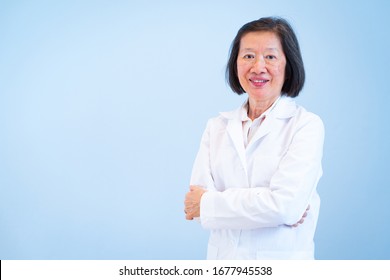 An Older Asian Woman Doctor Is Smiling And Wearing White Coat On The Blue Background