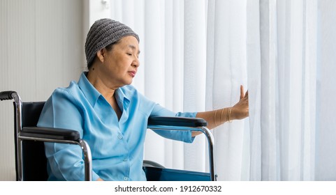 Older Asian Woman Patient Covered The Head With Clothes Effect From Chemo Treatment In Cancer Cure Process Lonely Sitting On Wheelchair And Wait For Someone To Visit Her.