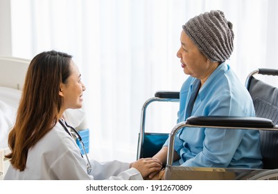 Older Asian Woman Patient Covered The Head With Clothes Effect From Chemo Treatment In Cancer Cure Process Sitting On Wheelchair And Talking To A Female Doctor.