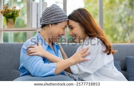 Older Asian woman patient covered the head with clothes effect from chemo treatment in cancer cure process touch her daughter's forehead with happy.