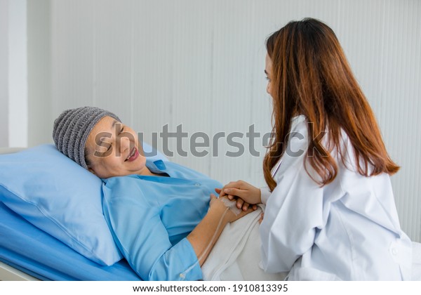 Older Asian woman patient covered the head with\
clothes effect from chemo treatment in cancer cure process talking\
to a female doctor.