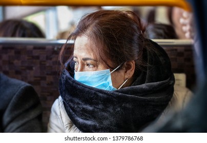 Older Asian Woman Wearing Black Fur Scarf And Surgical Pollution Mask Sitting On A Bus Train Subway In Fear Of Corona Virus COVID-19