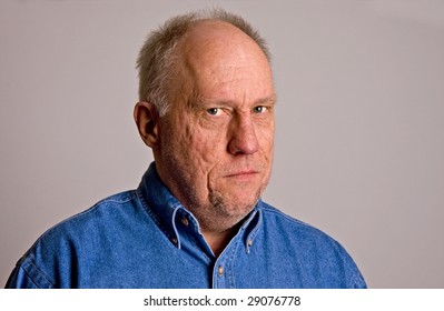 An Older Bald Man In A Blue Shirt On A Grey Background