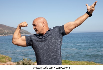 Older Bald Man Doing A Muscle Pose Flexing Biceps.