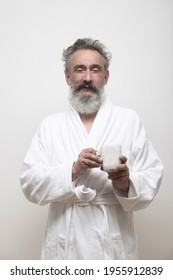 
Older Bearded Man With Bathrobe Looking At Camera  Holding A Mug On White Background