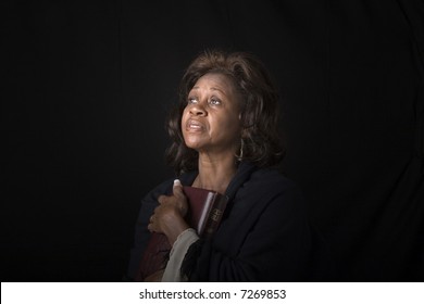 An older black woman clutching a bible and looking toward heaven