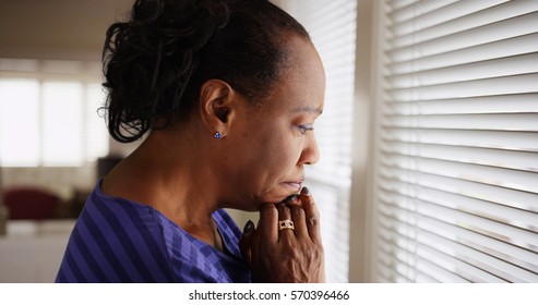 An older black woman mournfully looks out her window - Powered by Shutterstock