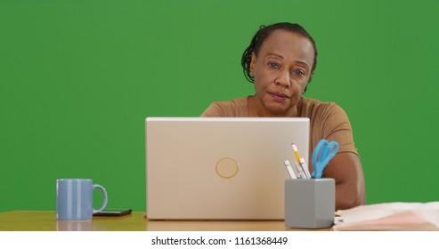 Older Black Woman Sitting At Desk With Laptop Looking At Camera On Green Screen