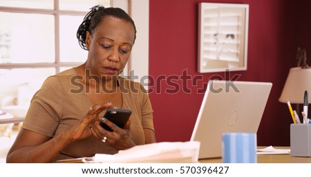 An older black woman uses her phone and laptop to do her taxes