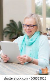 An Older Blonde Woman Operates A Tablet Computer While Sitting At Table Outside