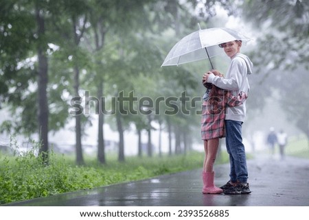 the older brother is carefully hiding his little sister from the rain under an umbrella