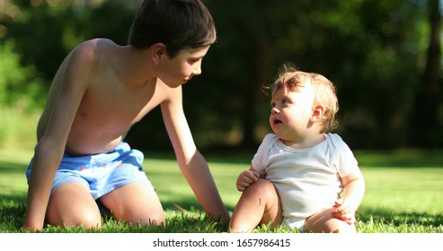 
Older Brother Caring For Baby Sibling. Authentic Family Moment. Two Brothers Together Outside In Garden