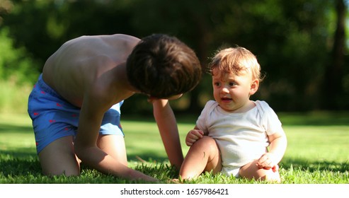 
Older Brother Caring For Baby Sibling. Authentic Family Moment. Two Brothers Together Outside In Garden