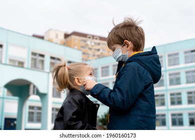Older brother dresses and corrects medical mask to younger sister before entering school, concept of protection from the spread of covid-19.