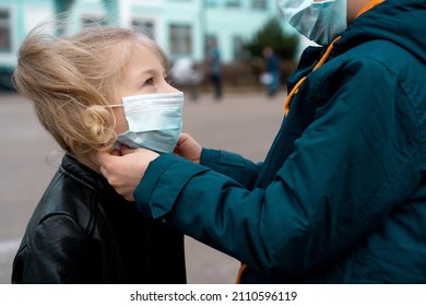 Older brother dresses and corrects medical mask to younger sister before entering school, concept of protection from the spread of covid-19