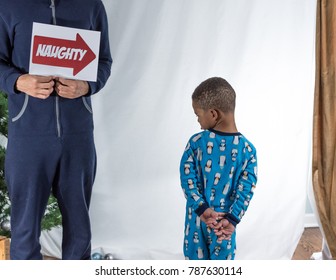 Older Brother Holding Up Sign Towards Toddler Brother Indicating He Is Naughty As He Throws A Tantrum.