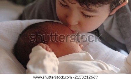 Older brother kisses newborn baby while he lies on bed