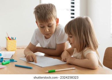 The older brother teaches the younger sister to read letters. The concept of brother and sister, home schooling. - Powered by Shutterstock