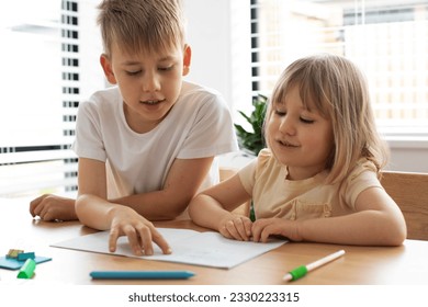 The older brother teaches the younger sister to read letters. The concept of brother and sister, home schooling. - Powered by Shutterstock