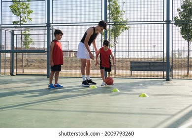 Older Brother Teaching How To Play Basketball To His Younger Siblings, One Of The Kids Has A Leg Prosthesis. Three Brothers Playing Basketball.