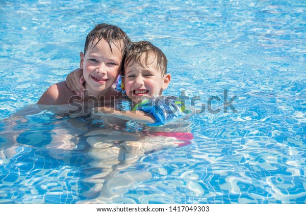 Older brother and younger brother swim in the\
outdoor children\'s pool