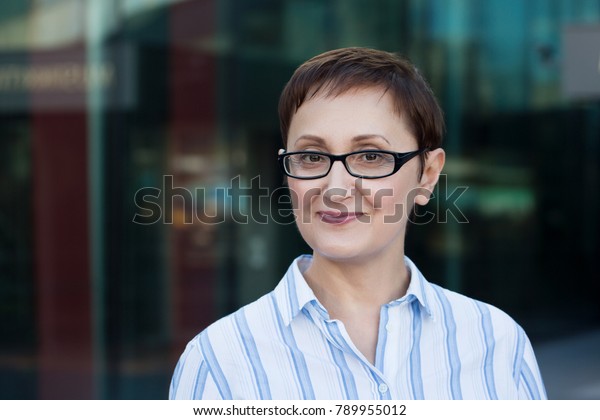 Older\
business woman headshot. Close-up portrait of executive, teacher,\
principal, CEO. Confident and successful middle aged woman 40 50\
years old wearing glasses and shirt and\
smiling